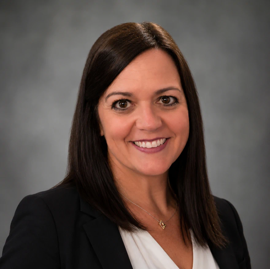 Woman with straight dark hair wearing a black blazer and white top, smiling at the camera against a gray background. Shauna Vasquez registered dental hygenist